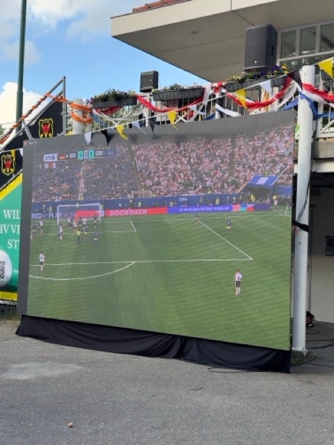 Groot outdoor LED scherm met voetbalwedstrijd op stadion met tribune zitplaatsen en feestelijke versiering erboven