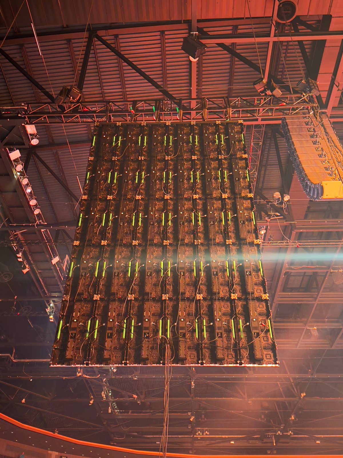 Industrial warehouse ceiling showing exposed metal beams, pipes, and yellow safety markings under warm orange lighting
