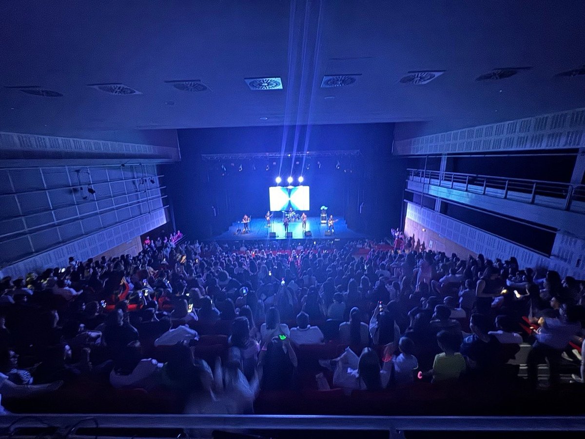 Large crowd at indoor concert venue with blue stage lighting and main screen display in center