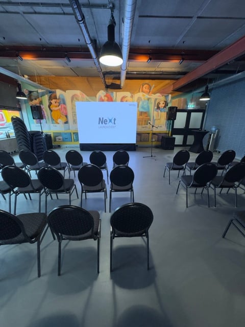 Empty presentation room with black chairs arranged around a projector screen displaying Next text